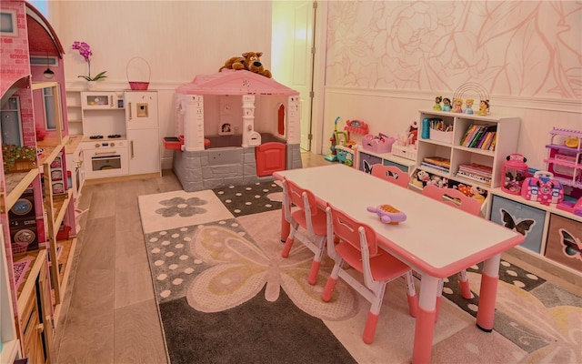 recreation room featuring wallpapered walls, light wood-style flooring, and a decorative wall