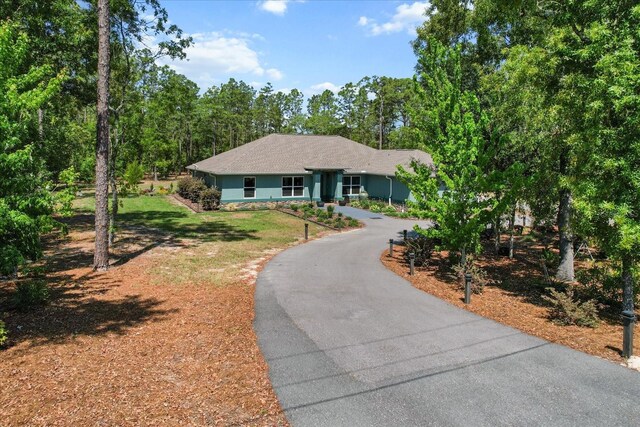 ranch-style house with driveway, roof with shingles, and a front lawn