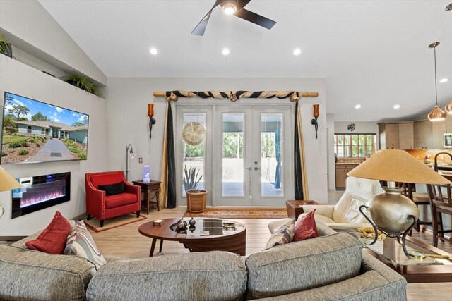 living room with a glass covered fireplace, ceiling fan, recessed lighting, french doors, and light wood-style flooring