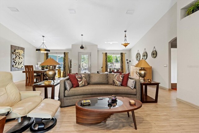 living area featuring visible vents, arched walkways, baseboards, light wood-type flooring, and vaulted ceiling