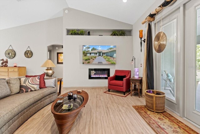 living area with a glass covered fireplace, arched walkways, vaulted ceiling, and wood finished floors