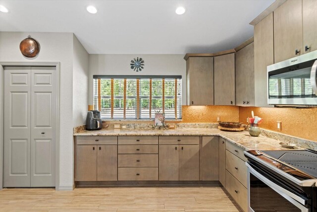 kitchen featuring light wood finished floors, stainless steel microwave, range with electric cooktop, and light stone countertops