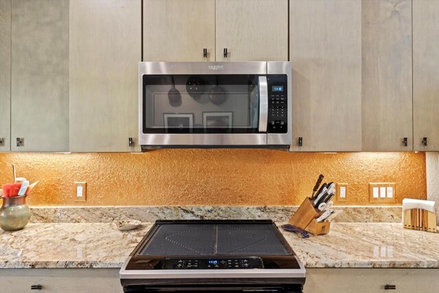 kitchen featuring backsplash, stainless steel microwave, light stone counters, and range with electric stovetop