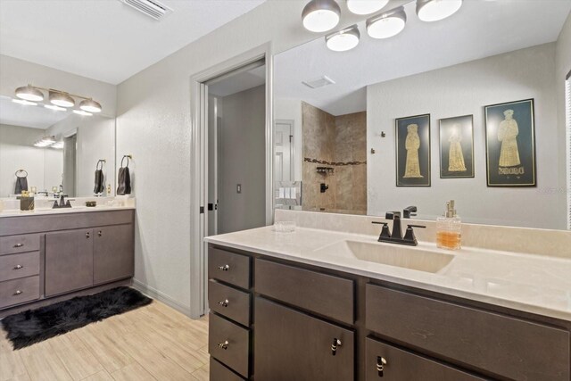 bathroom with visible vents, a sink, two vanities, and tiled shower