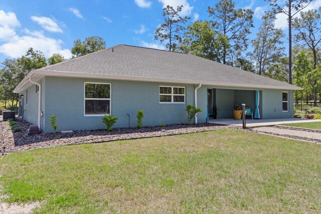 view of front of house featuring roof with shingles, a front lawn, stucco siding, central air condition unit, and a carport
