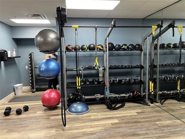 workout area with visible vents, baseboards, a paneled ceiling, and wood finished floors