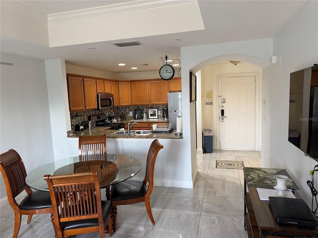 kitchen featuring baseboards, brown cabinets, tasteful backsplash, arched walkways, and stainless steel appliances