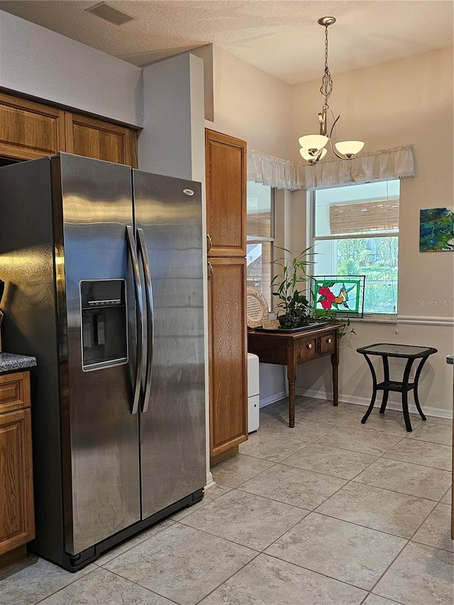 kitchen featuring brown cabinets, an inviting chandelier, stainless steel fridge, decorative light fixtures, and visible vents