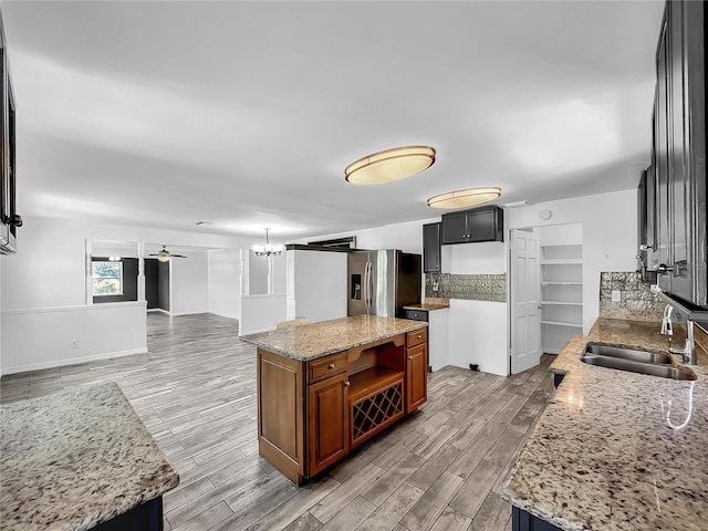 kitchen featuring light stone counters, a sink, decorative backsplash, wood tiled floor, and stainless steel refrigerator with ice dispenser