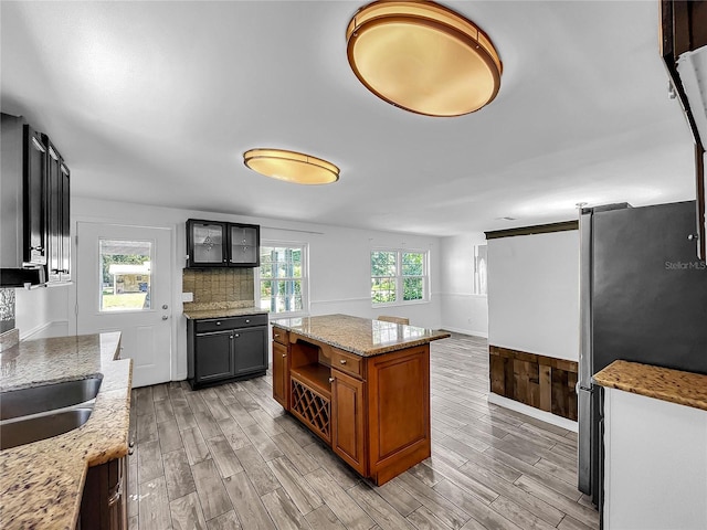kitchen with freestanding refrigerator, light stone counters, a center island, and light wood-type flooring