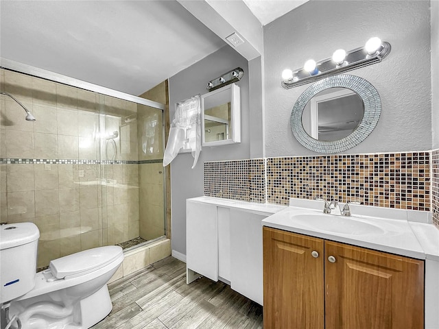 bathroom with backsplash, a stall shower, wood finished floors, vanity, and toilet