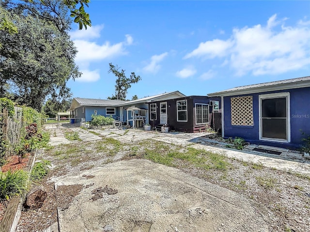 rear view of house featuring stucco siding, fence, and metal roof