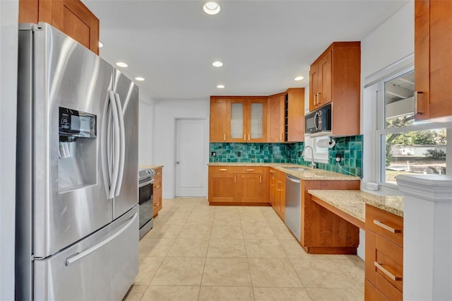 1231 Glastonberry Rd, Maitland, FL 32751 - kitchen with brown cabinets, light stone counters, stainless steel appliances, decorative backsplash, and glass insert cabinets