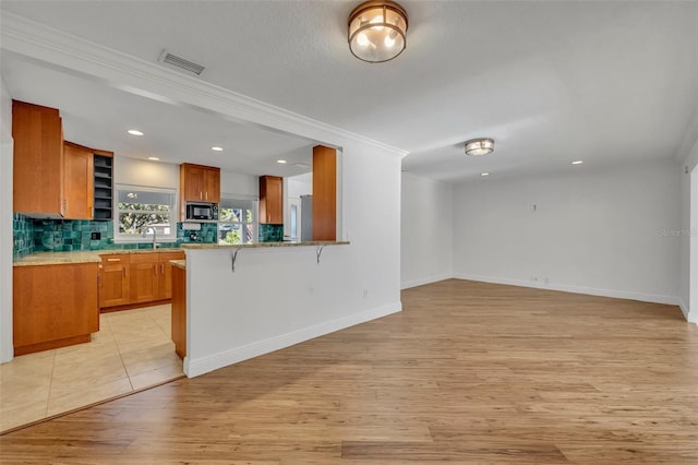 1231 Glastonberry Rd, Maitland, FL 32751 - kitchen with brown cabinetry, black microwave, open floor plan, a breakfast bar area, and light wood-style flooring