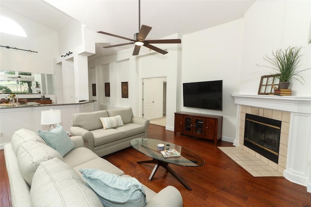 living area with high vaulted ceiling, ceiling fan, a fireplace, and wood finished floors