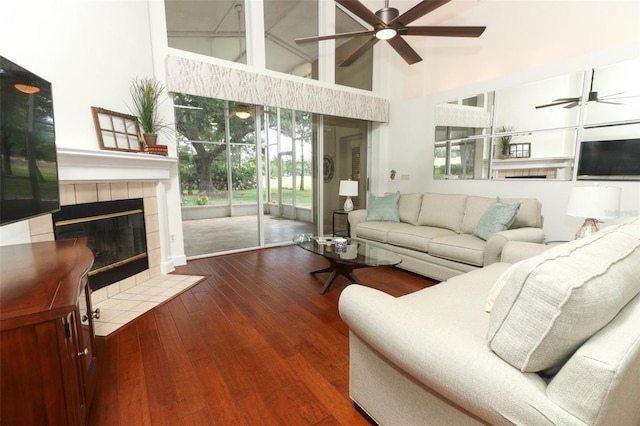 living area featuring ceiling fan, hardwood / wood-style flooring, a tiled fireplace, and high vaulted ceiling