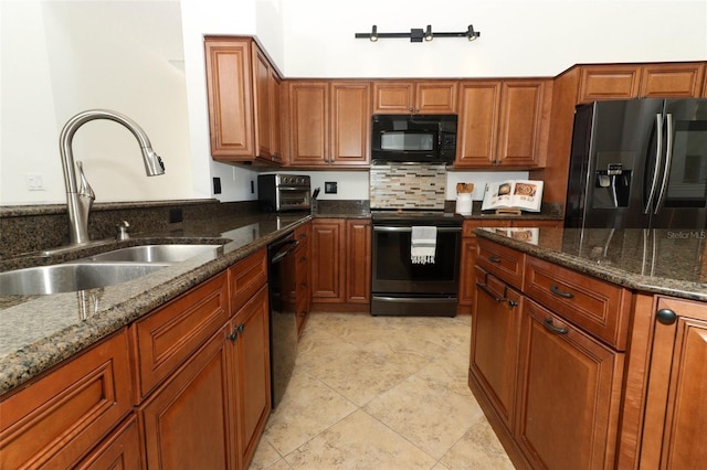 kitchen with a sink, brown cabinets, black appliances, and dark stone countertops