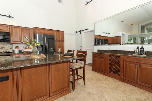 kitchen featuring appliances with stainless steel finishes, a high ceiling, brown cabinets, and a barn door