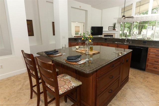 kitchen with a kitchen breakfast bar, black dishwasher, dark stone counters, a tile fireplace, and a sink