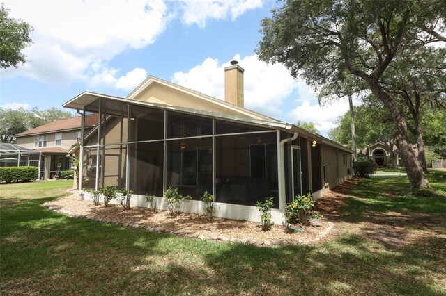 back of house featuring a lawn, a chimney, and a sunroom