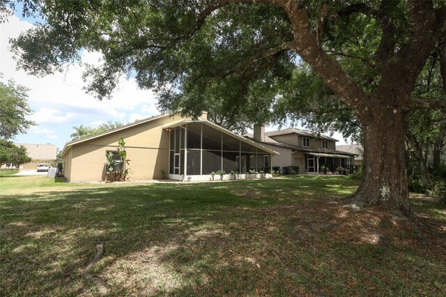 rear view of house with a lawn, a sunroom, and stucco siding