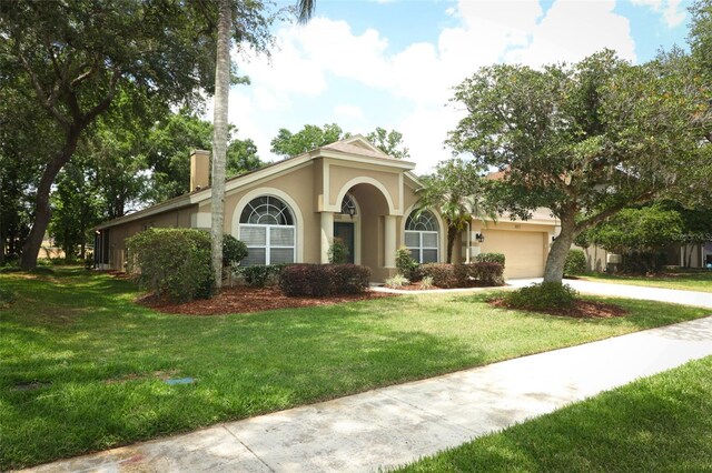 view of front of home featuring an attached garage, stucco siding, a front yard, a chimney, and concrete driveway