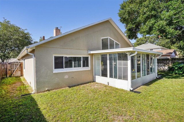 back of property with fence, stucco siding, a chimney, a sunroom, and a lawn