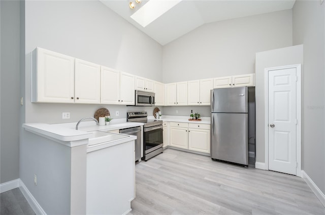 kitchen featuring high vaulted ceiling, white cabinets, a sink, a skylight, and stainless steel appliances
