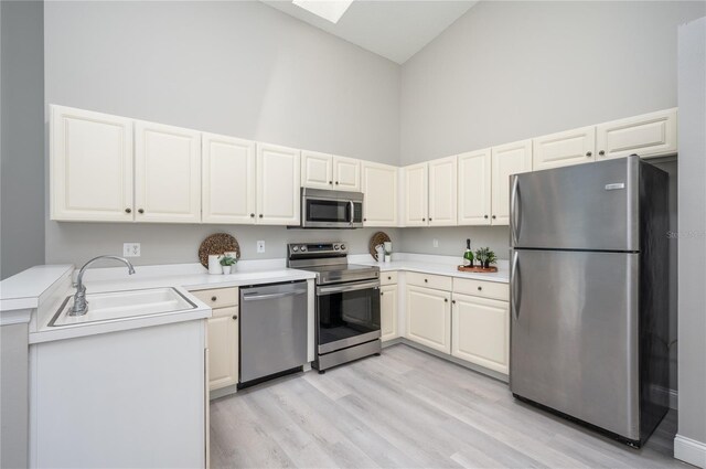 kitchen featuring light wood-style floors, high vaulted ceiling, light countertops, a sink, and appliances with stainless steel finishes