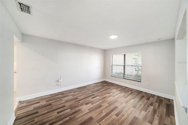 empty room featuring baseboards, dark wood-type flooring, a textured ceiling, and visible vents