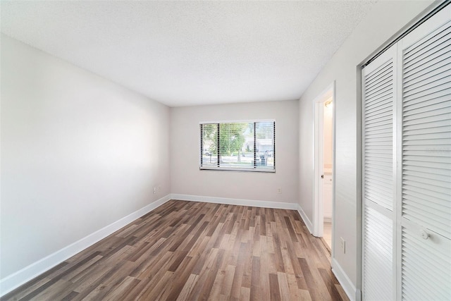 unfurnished bedroom with a textured ceiling, baseboards, a closet, and wood finished floors