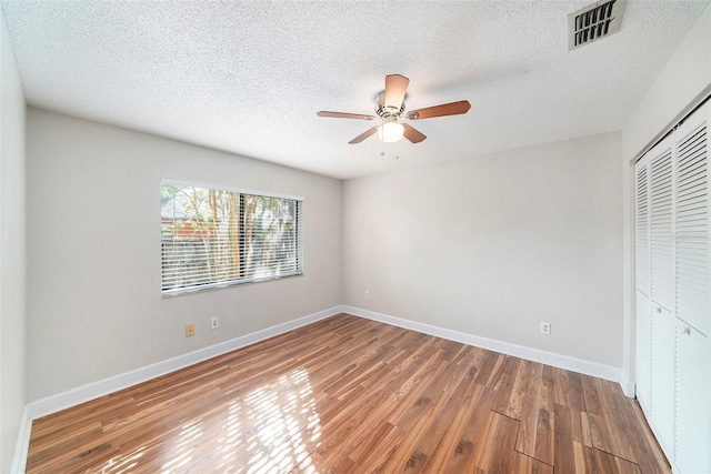 unfurnished bedroom featuring a textured ceiling, baseboards, wood finished floors, visible vents, and a closet