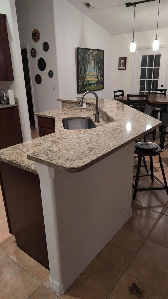 kitchen featuring a sink, light tile patterned floors, a center island with sink, and decorative light fixtures