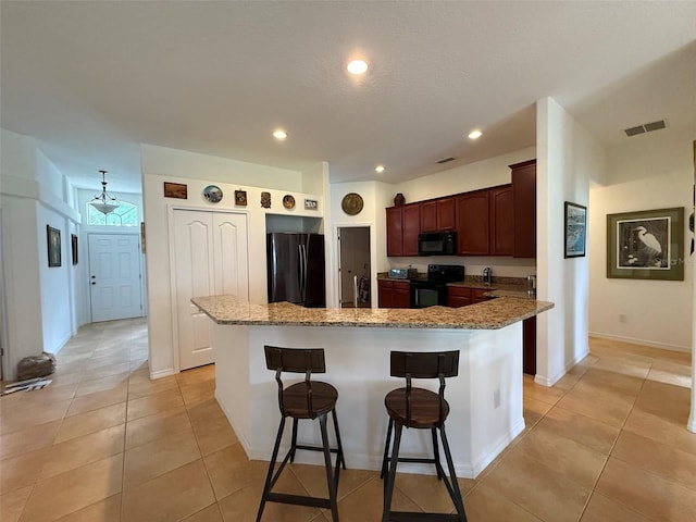 4920 E Lake Cove Blvd, Saint Cloud, FL 34771 - kitchen with black appliances, a breakfast bar area, light tile patterned floors, light stone countertops, and a center island
