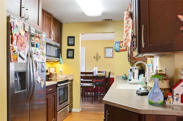 kitchen featuring appliances with stainless steel finishes, a sink, light wood finished floors, light countertops, and visible vents