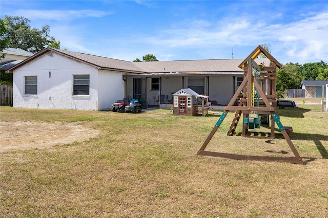 back of house with a playground, stucco siding, and a lawn