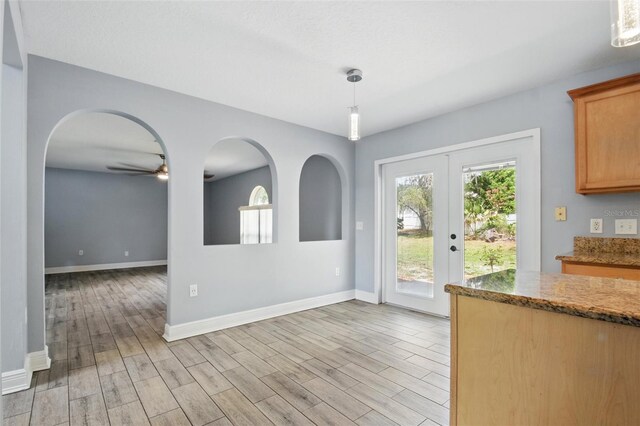 unfurnished dining area featuring baseboards, a ceiling fan, light wood-style floors, and arched walkways