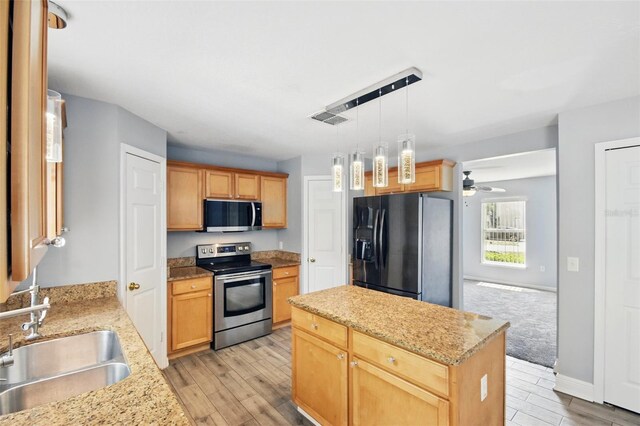 kitchen with appliances with stainless steel finishes, a sink, light wood finished floors, and a center island