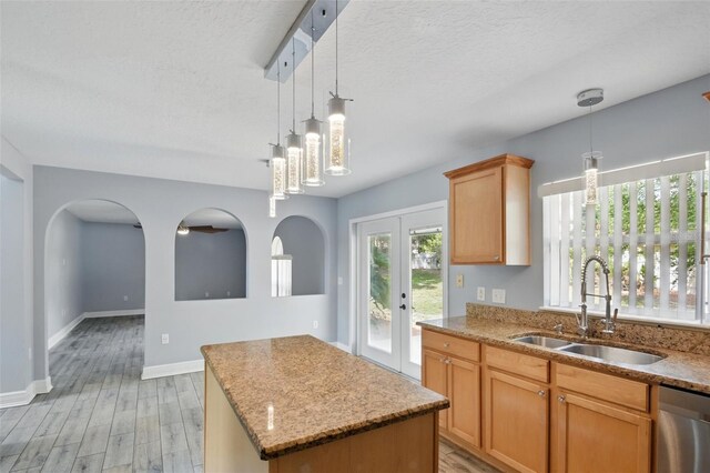 kitchen featuring a kitchen island, stainless steel dishwasher, light stone countertops, a sink, and light wood-style flooring