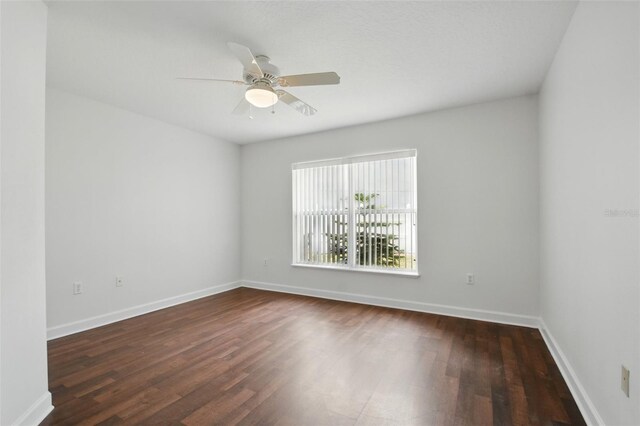spare room featuring ceiling fan, dark wood-style floors, and baseboards
