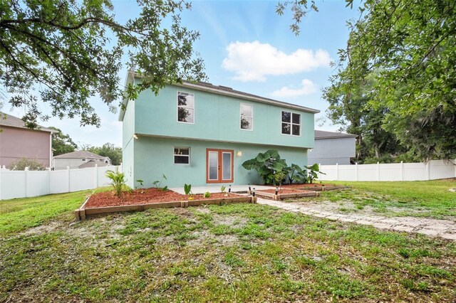 rear view of property with french doors, a fenced backyard, a lawn, and a garden