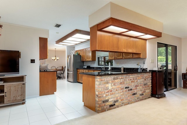 kitchen with a peninsula, brown cabinetry, freestanding refrigerator, visible vents, and dark countertops