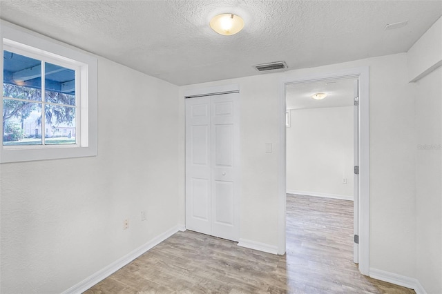 unfurnished bedroom featuring baseboards, light wood-type flooring, a textured ceiling, and visible vents