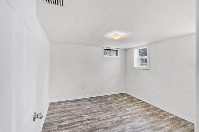 below grade area with visible vents, baseboards, a textured ceiling, and wood finished floors