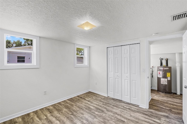unfurnished bedroom featuring visible vents, a textured ceiling, wood finished floors, and electric water heater
