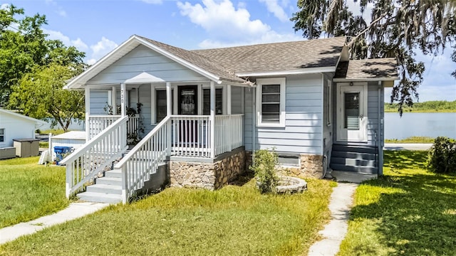 bungalow-style home featuring roof with shingles, a water view, and a front lawn