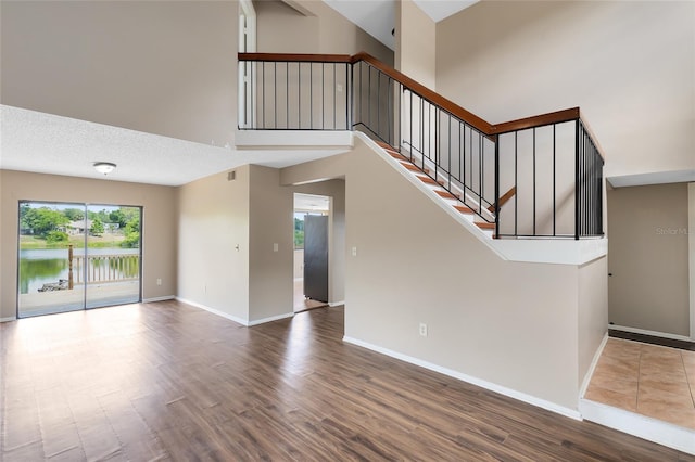 unfurnished living room featuring stairs, a water view, baseboards, and wood finished floors