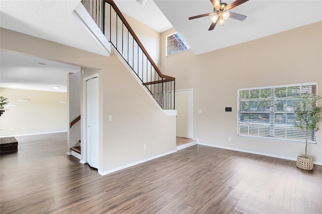 unfurnished living room featuring ceiling fan, wood finished floors, stairway, baseboards, and a high ceiling