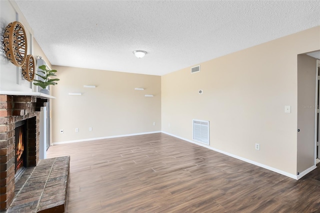 unfurnished living room featuring visible vents, a textured ceiling, a brick fireplace, and wood finished floors