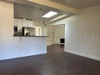 kitchen featuring baseboards, a peninsula, dark countertops, and stainless steel fridge with ice dispenser